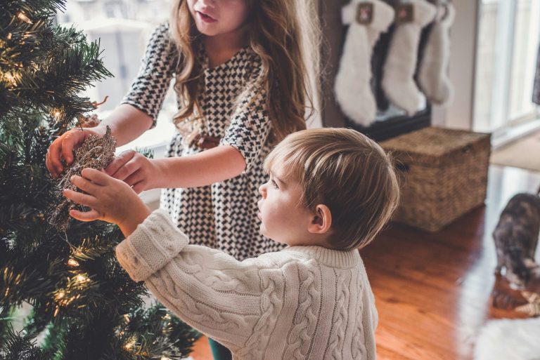 Christmas Giving Ideas for Families - two kids putting ornaments on tree