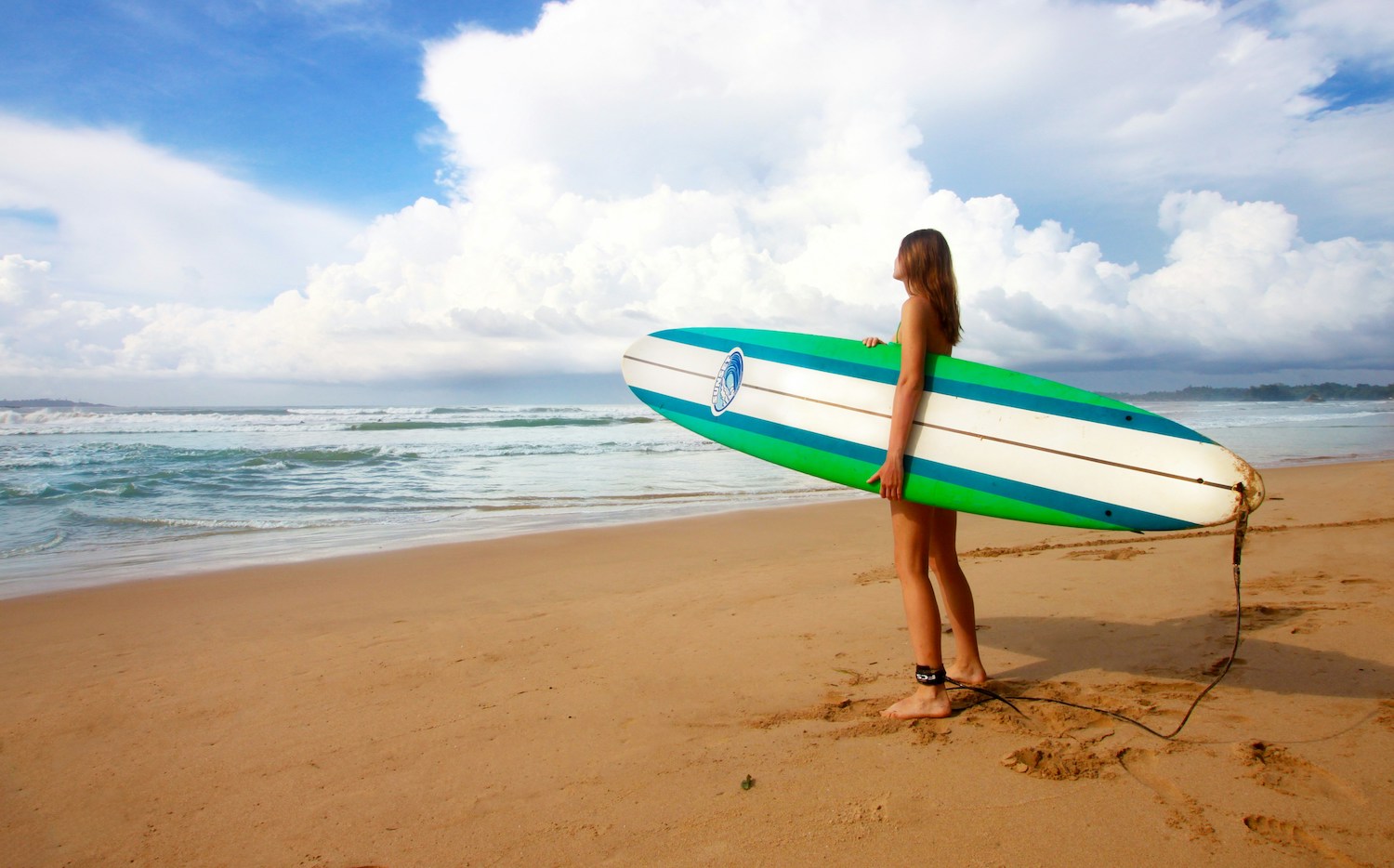 Girl standing on beach with surfboard