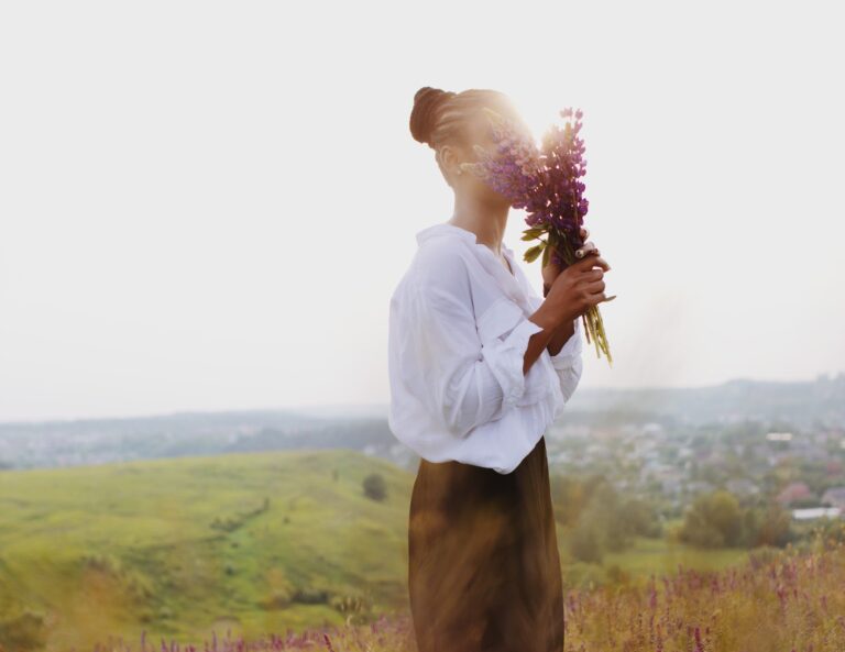 Woman in white shirt standing in a field holding flowers