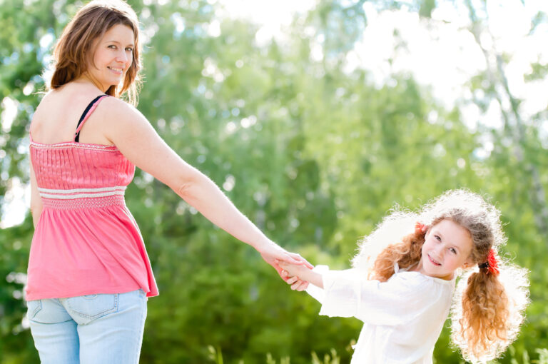 Mom and young daughter holding hands outside in summer