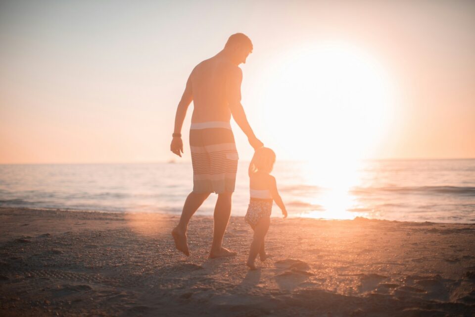 Dad holding child's hand on the beach offering Father’s Day Ideas