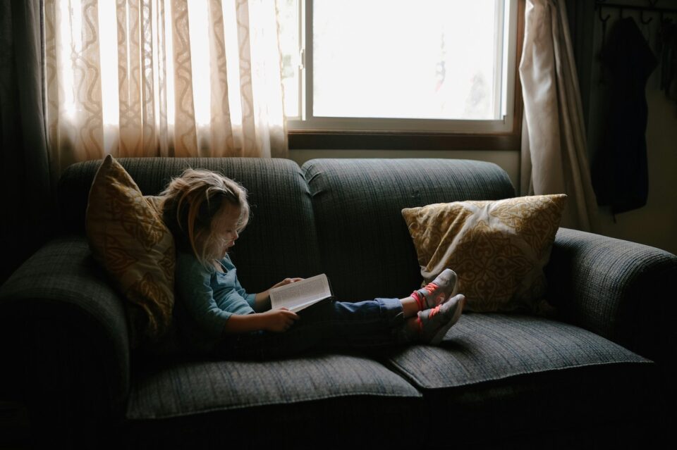 Little girl sitting on couch reading a book