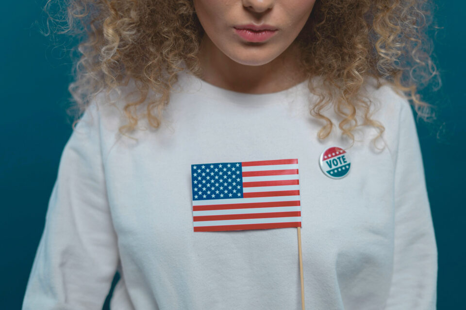 Woman with curly hair wearing voting pin and American flag