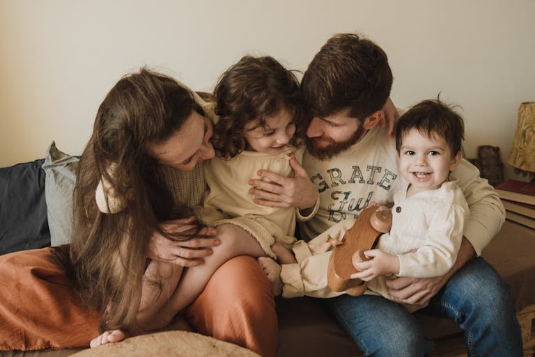 A joyful family moment with parents and children embracing and laughing together indoors.