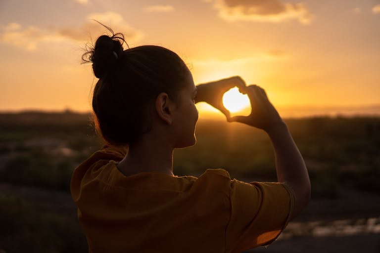 A silhouette of a young woman forming a heart shape at sunset no motherhood stress