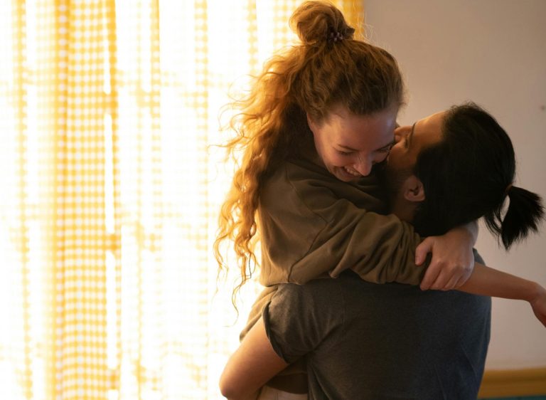 Become a better love - Joyful moment of a couple hugging in their cozy, sunlit living room.