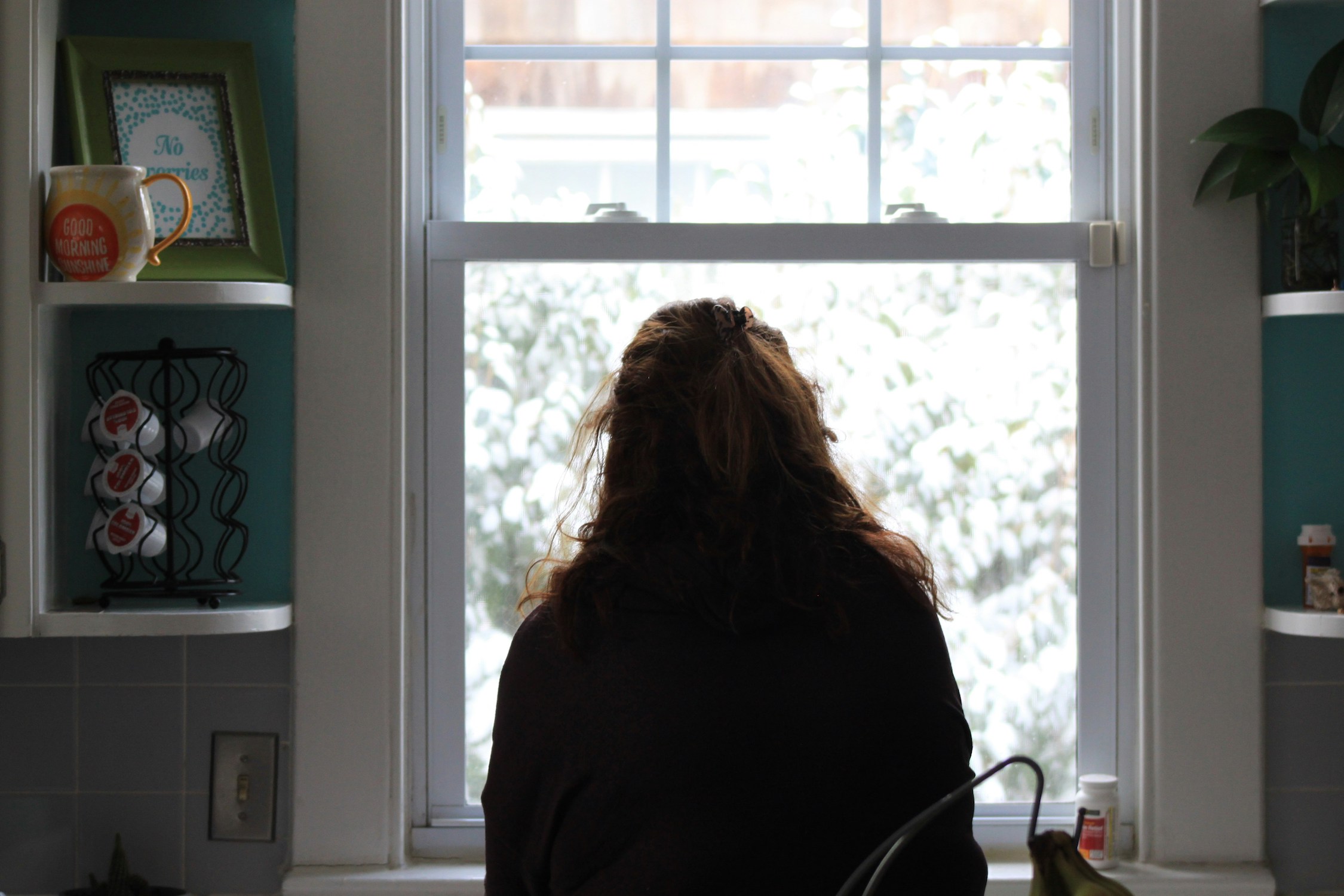 Woman looking out kitchen window dealing with the exhaustion of motherhood