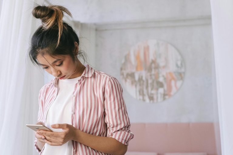 Woman in pink shirt scrolling phone when comparison steals your joy