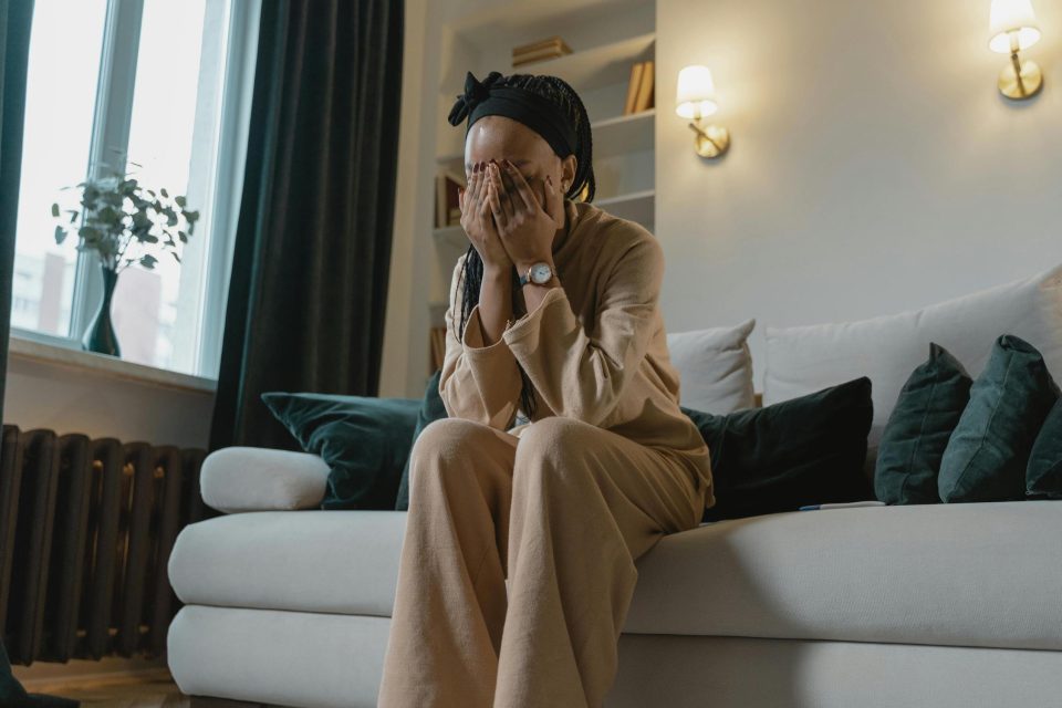 Woman sitting on couch covering face who is parenting through health challenges