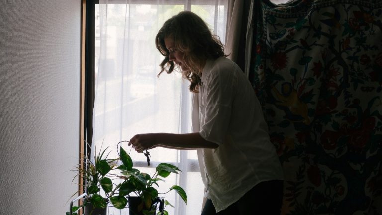 Woman in shadows watering plants and creating household systems