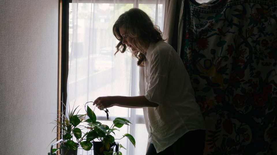 Woman in shadows watering plants and creating household systems